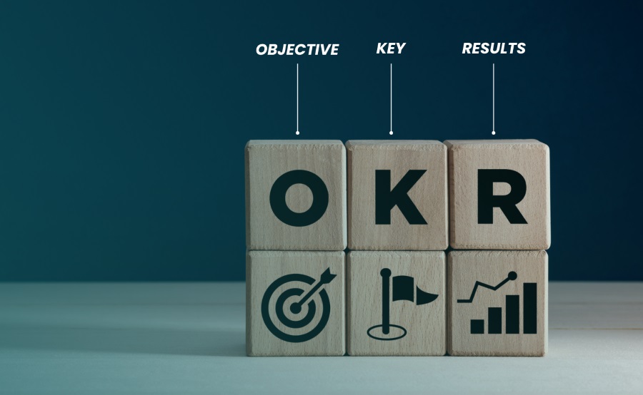 Stack of wooden blocks labeled O, K, and R with icons for objective, key, and results—illustrating the OKR goal-setting framework in business strategy.